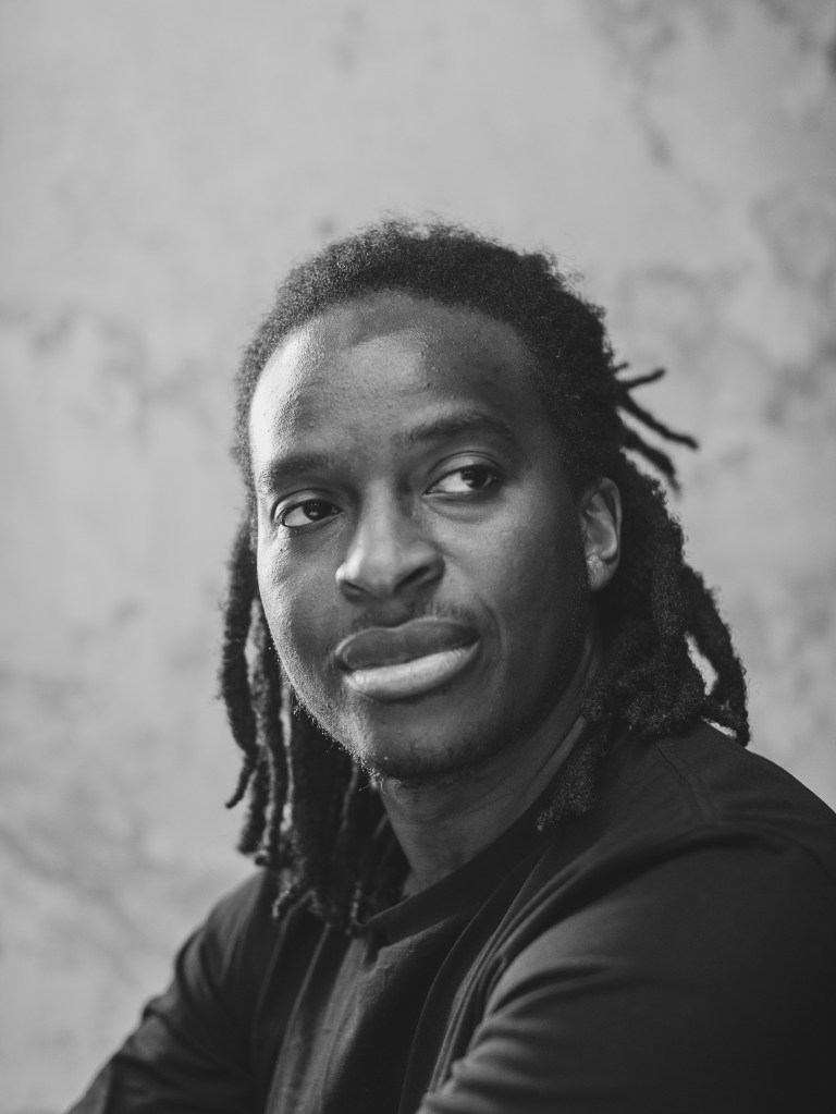 This is a black and white portrait of the poet, Kayo Chingonyi looking out of frame, a contemplative expression on his face.